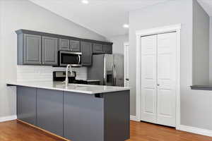 Kitchen with vaulted ceiling, hardwood / wood-style flooring, decorative backsplash, appliances with stainless steel finishes, and kitchen peninsula