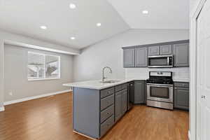 Kitchen featuring decorative backsplash, stainless steel appliances, kitchen peninsula, and gray cabinetry