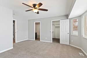 Unfurnished bedroom featuring a walk in closet, light colored carpet, ceiling fan, connected bathroom, and a closet