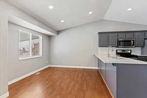 Kitchen featuring gray cabinetry, lofted ceiling, sink, tasteful backsplash, and stainless steel appliances