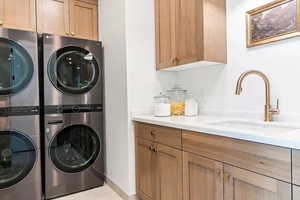 Clothes washing area with stacked washer / dryer, sink, light tile patterned floors, and cabinets