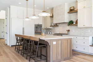 Kitchen featuring a kitchen bar, backsplash, decorative light fixtures, a center island with sink, and white cabinets