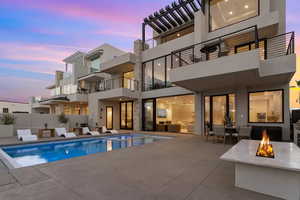 Back house at dusk featuring a fenced in pool, a patio, and an outdoor fire pit