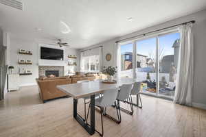 Dining space featuring ceiling fan, light hardwood / wood-style flooring, a textured ceiling, and a brick fireplace