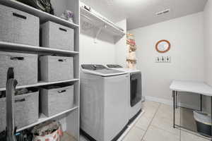 Washroom featuring washing machine and dryer, light tile patterned floors, and a textured ceiling