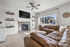 Living room featuring ceiling fan, a fireplace, and light hardwood / wood-style flooring