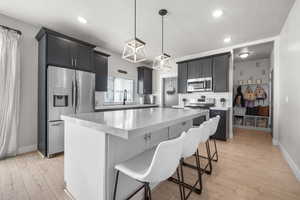 Kitchen with decorative backsplash, appliances with stainless steel finishes, a kitchen breakfast bar, a center island, and hanging light fixtures