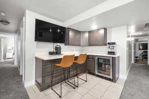 Kitchen with a breakfast bar, dark brown cabinets, light colored carpet, and beverage cooler