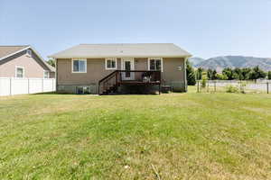 Back of property with a deck with mountain view and a lawn