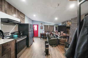 Kitchen with light wood-type flooring, a textured ceiling, vaulted ceiling, wooden walls, and electric stove