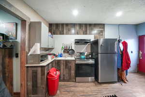 Kitchen with stainless steel appliances, light hardwood / wood-style flooring, a textured ceiling, white cabinets, and exhaust hood