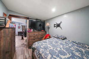 Bedroom with a barn door, light wood-type flooring, and lofted ceiling