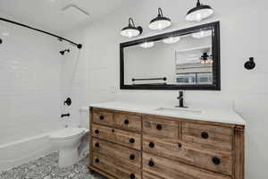 Full bathroom with vanity, tiled shower / bath combo, ceiling fan, tile patterned flooring, and toilet