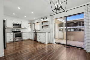 Kitchen with pendant lighting, dark hardwood / wood-style floors, appliances with stainless steel finishes, a notable chandelier, and white cabinetry