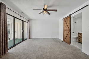 Empty room with a barn door, ceiling fan, and light colored carpet