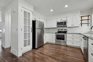 Kitchen with white cabinetry, sink, dark wood-type flooring, backsplash, and appliances with stainless steel finishes