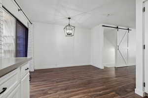 Unfurnished dining area with a barn door, dark wood-type flooring, and a chandelier