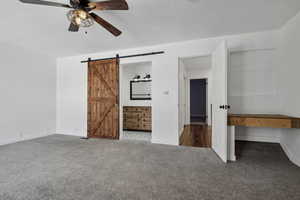 Unfurnished bedroom with carpet, a barn door, and ceiling fan