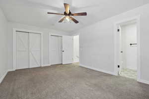 Unfurnished bedroom featuring carpet flooring, ceiling fan, and multiple closets