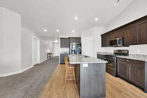 Kitchen featuring a kitchen island with sink, sink, light stone countertops, light hardwood / wood-style floors, and stainless steel appliances