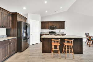 Kitchen with light stone countertops, sink, an island with sink, lofted ceiling, and appliances with stainless steel finishes