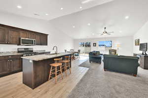 Kitchen featuring stove, a kitchen breakfast bar, ceiling fan, sink, and an island with sink