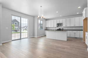 Kitchen with stainless steel appliances, pendant lighting, an inviting chandelier, white cabinets, and light hardwood / wood-style floors