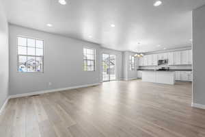 Unfurnished living room featuring a textured ceiling, light hardwood / wood-style floors, sink, and an inviting chandelier