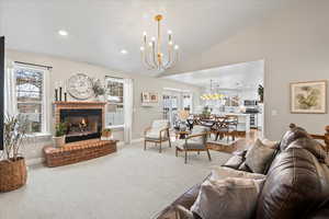 Living room with vaulted ceiling, a healthy amount of sunlight, a notable chandelier, and a brick fireplace