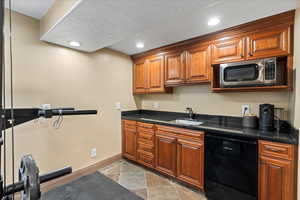 Basement bar featuring a textured ceiling, dishwasher, dark stone countertops, and sink