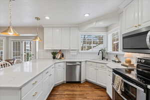 Kitchen with hanging light fixtures, sink, kitchen peninsula, appliances with stainless steel finishes, and white cabinetry