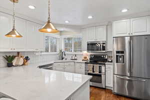 Kitchen with sink, hanging light fixtures, decorative backsplash, white cabinetry, and stainless steel appliances