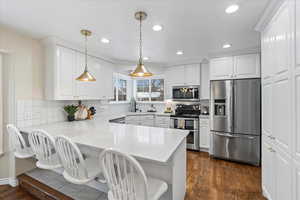 Kitchen with pendant lighting, white cabinets, appliances with stainless steel finishes, a kitchen bar, and kitchen peninsula