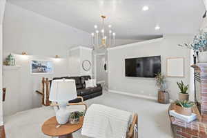 Living room with carpet, lofted ceiling, an inviting chandelier, ornamental molding, and a fireplace