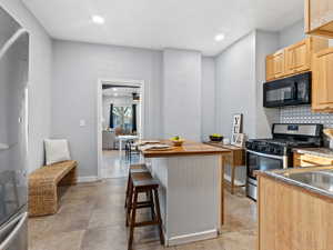 Kitchen featuring a breakfast bar, light brown cabinets, stainless steel gas range, decorative backsplash, and fridge