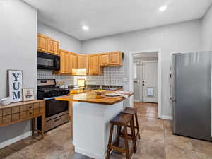 Kitchen featuring wooden counters, light brown cabinetry, a breakfast bar, stainless steel appliances, and a kitchen island