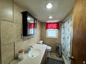 Bathroom featuring a textured ceiling, vanity, tile walls, and a shower with shower curtain