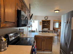 Kitchen featuring kitchen peninsula, a textured ceiling, electric range oven, and stainless steel refrigerator