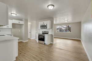 Kitchen with white cabinetry, sink, stainless steel appliances, a textured ceiling, and light wood-type flooring