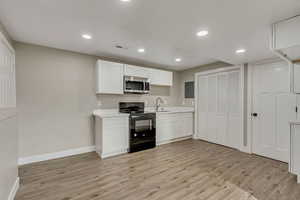 Kitchen with electric range, white cabinets, sink, and light hardwood / wood-style flooring