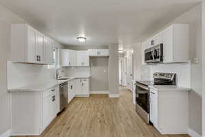 Kitchen featuring sink, decorative backsplash, appliances with stainless steel finishes, light hardwood / wood-style floors, and white cabinetry