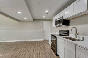 Kitchen featuring white cabinets, black range with electric stovetop, sink, light stone countertops, and light hardwood / wood-style floors