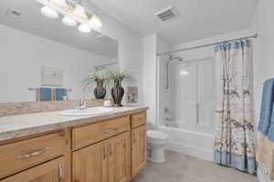 Full bathroom with a textured ceiling, vanity, toilet, and shower / bathtub combination with curtain