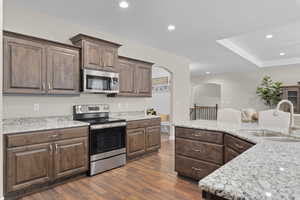 Kitchen with dark hardwood / wood-style floors, light stone countertops, sink, and appliances with stainless steel finishes