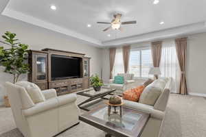 Living room with ceiling fan, a raised ceiling, and light colored carpet