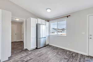 Unfurnished bedroom with lofted ceiling, stainless steel fridge, and light wood-type flooring