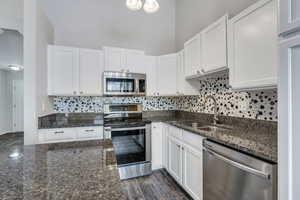 Kitchen featuring dark stone countertops, white cabinetry, and appliances with stainless steel finishes