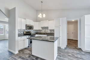 Kitchen featuring an inviting chandelier, decorative backsplash, dark stone countertops, white cabinetry, and stainless steel appliances