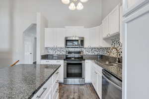 Kitchen featuring decorative backsplash, sink, white cabinets, and stainless steel appliances