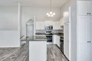 Kitchen featuring decorative backsplash, stainless steel appliances, white cabinets, a kitchen island, and hanging light fixtures